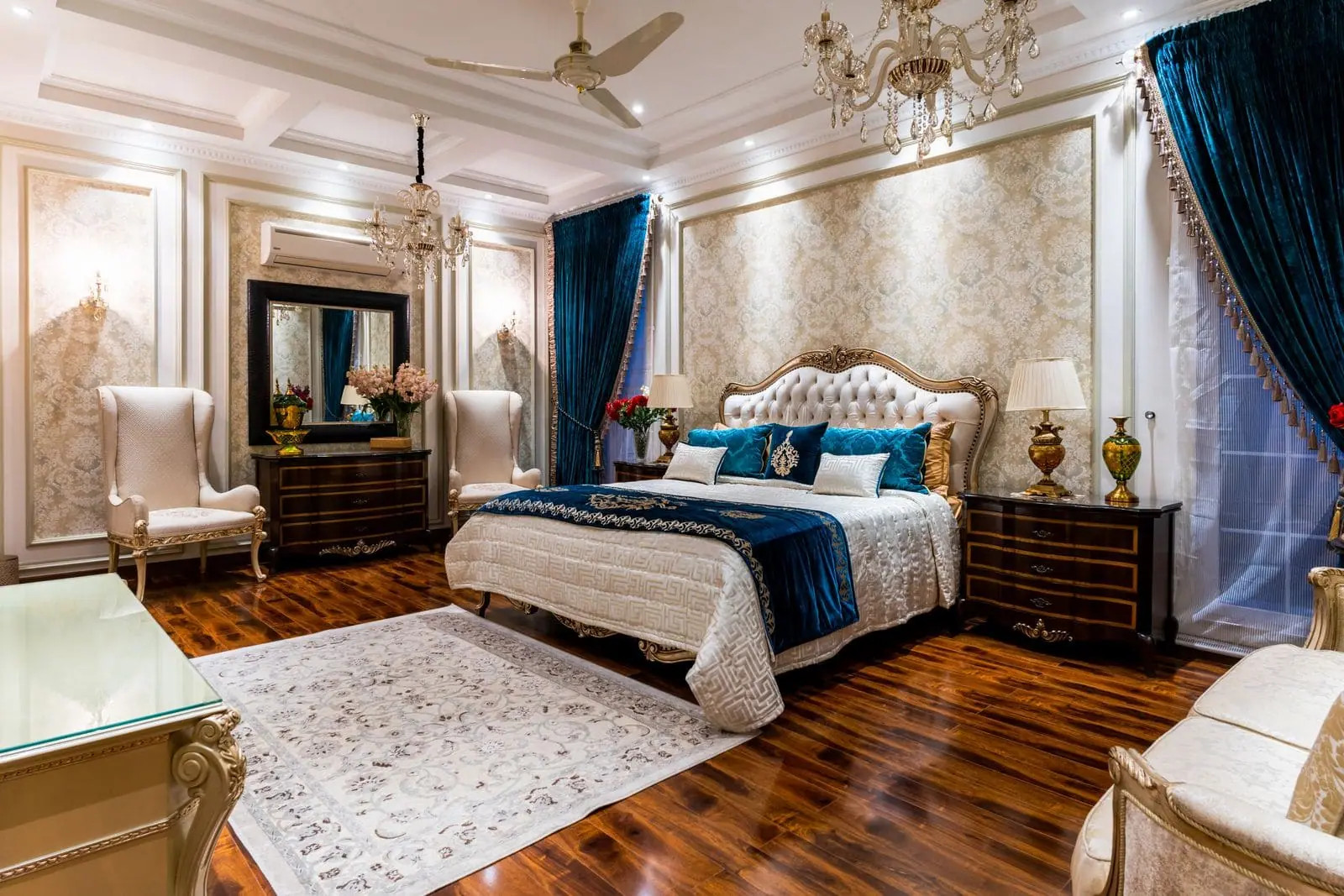 Classic bedroom with a tufted headboard, panelled walls, chandelier and blue velvet curtains