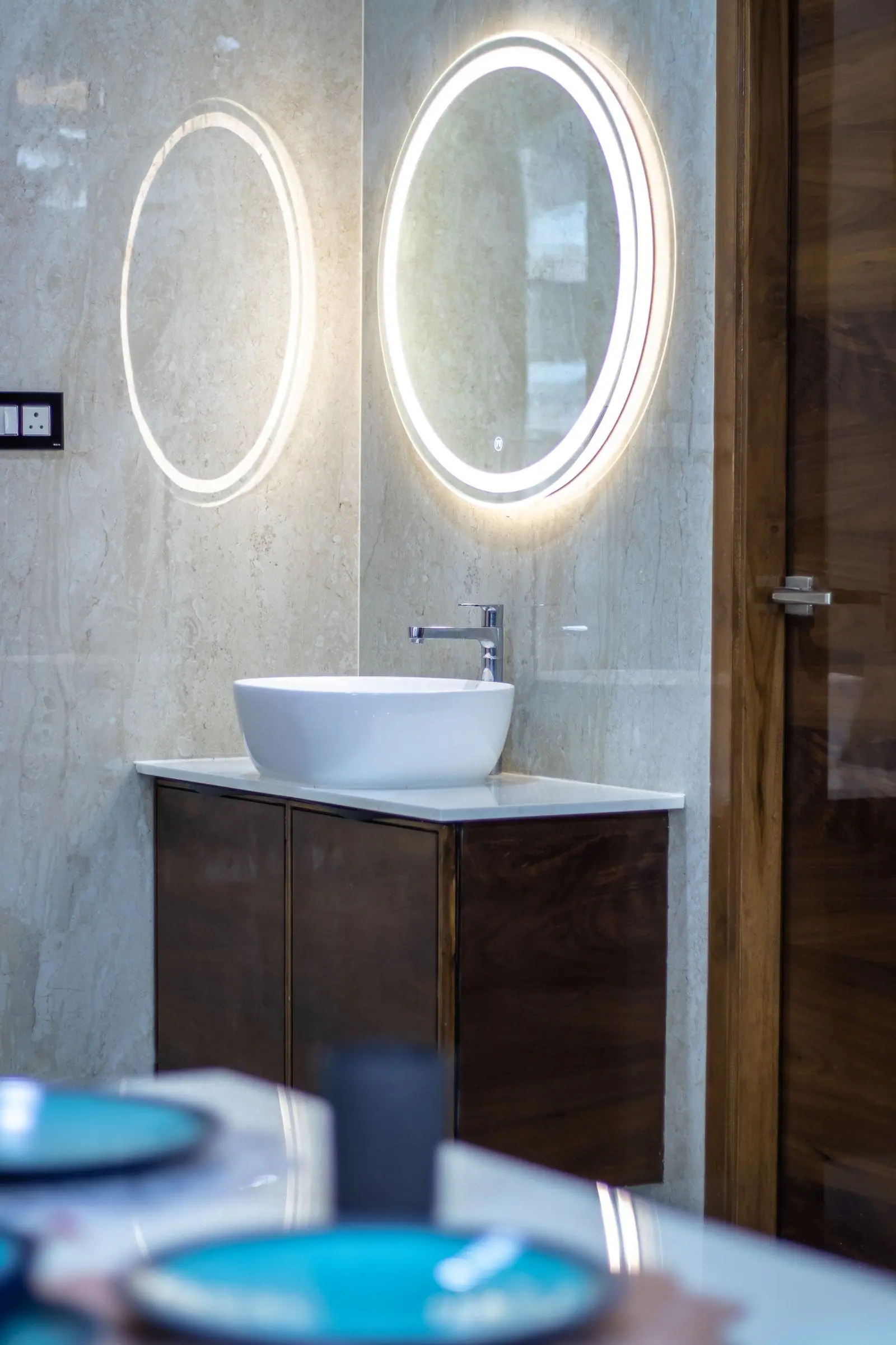 Bathroom vanity in dark wood with a vessel basin and backlit round mirrors