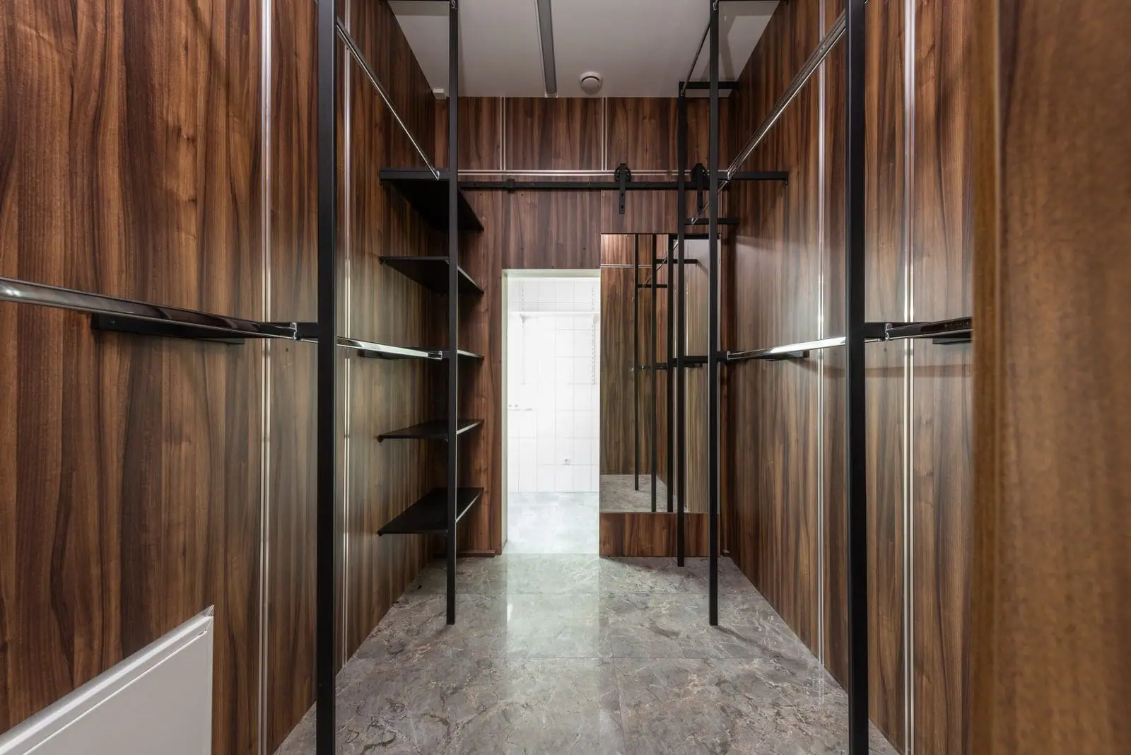 Walk-in wardrobe lined with walnut panelling and slim black hanging rails